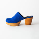 Blue suede clog shoe with wooden sole on a white background