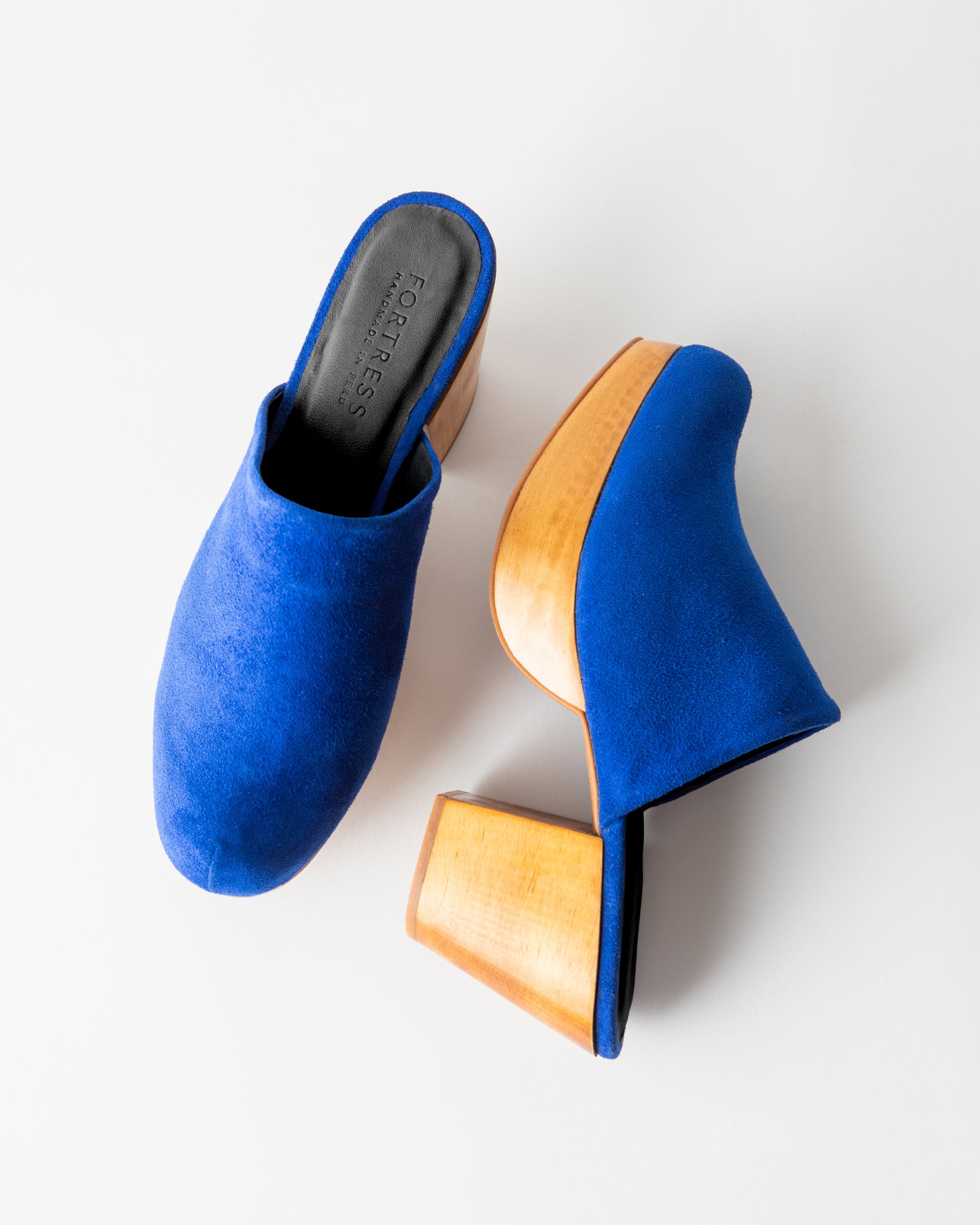 Blue suede mules with wooden soles on a white background