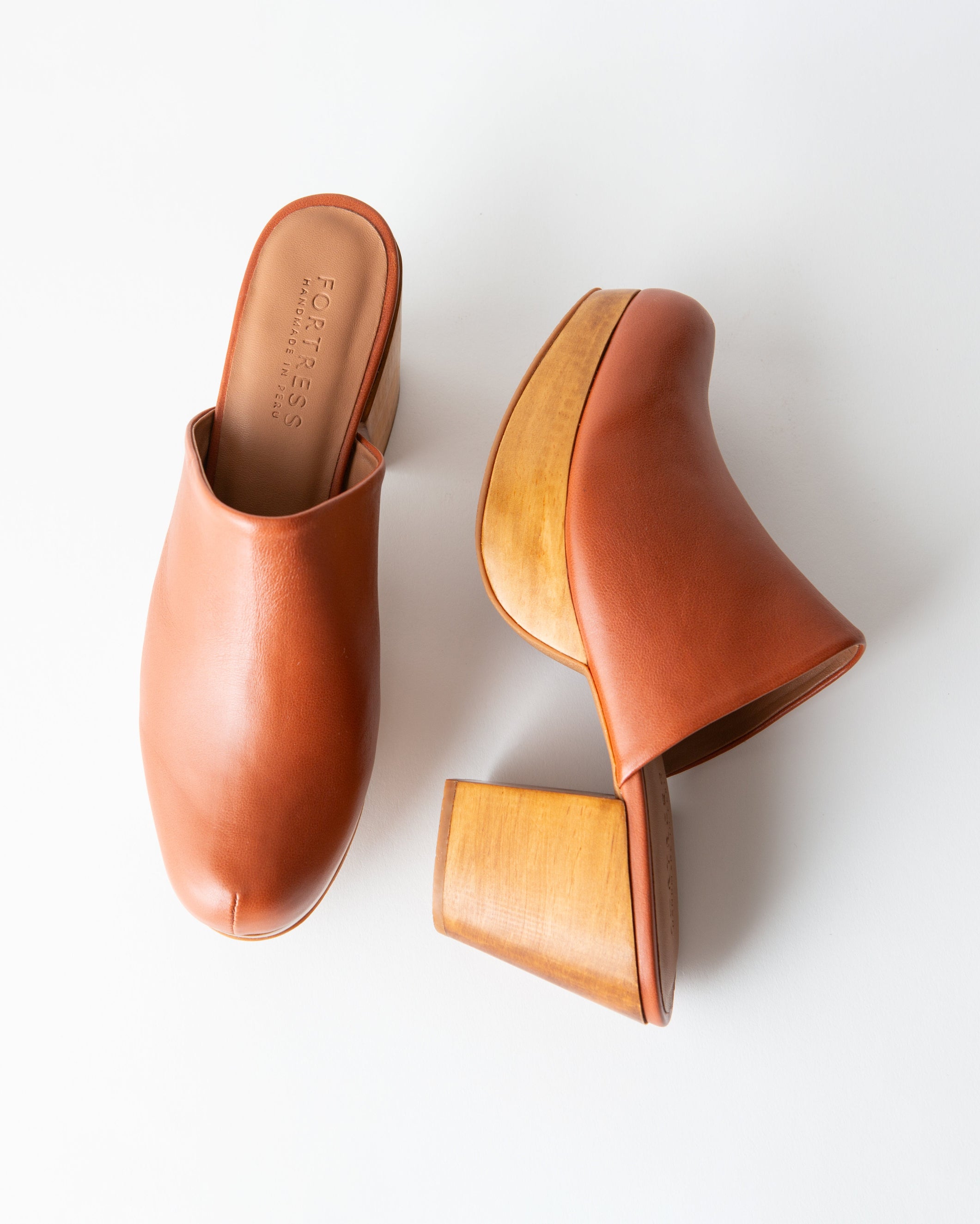 Pair of brown leather mules with a wood platform on a white background