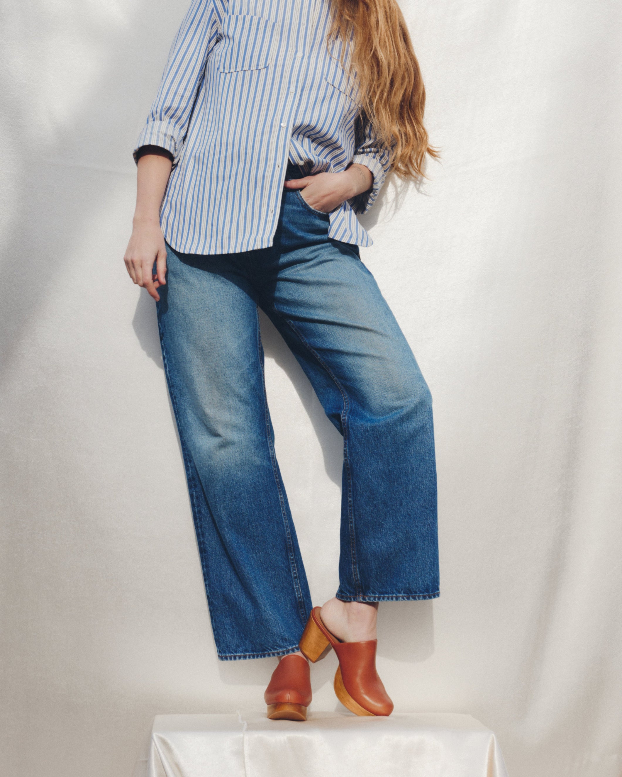 Model wearing a striped shirt, blue jeans, and brown clog mules on a white background