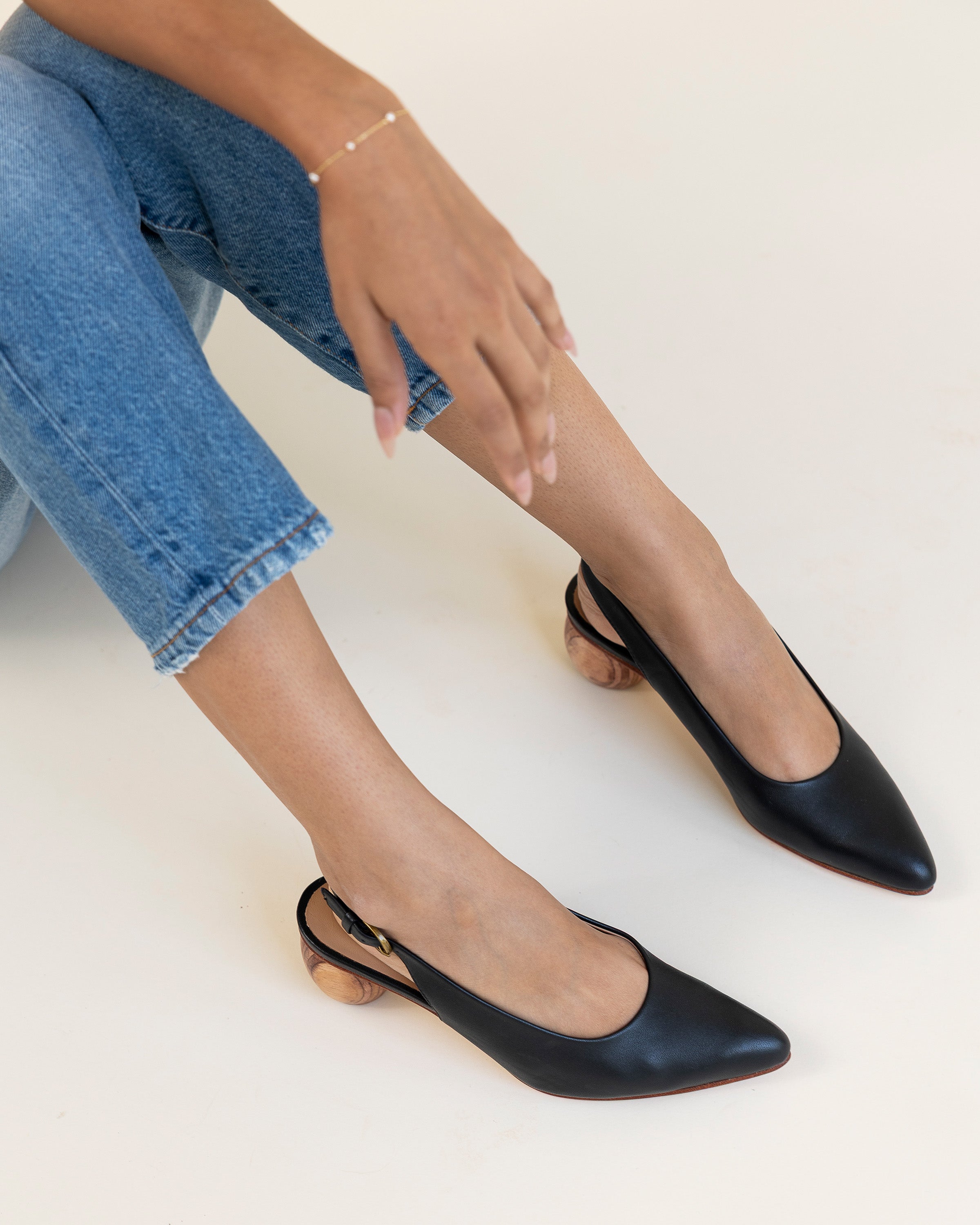 Black slingback shoes worn with blue jeans on a white background