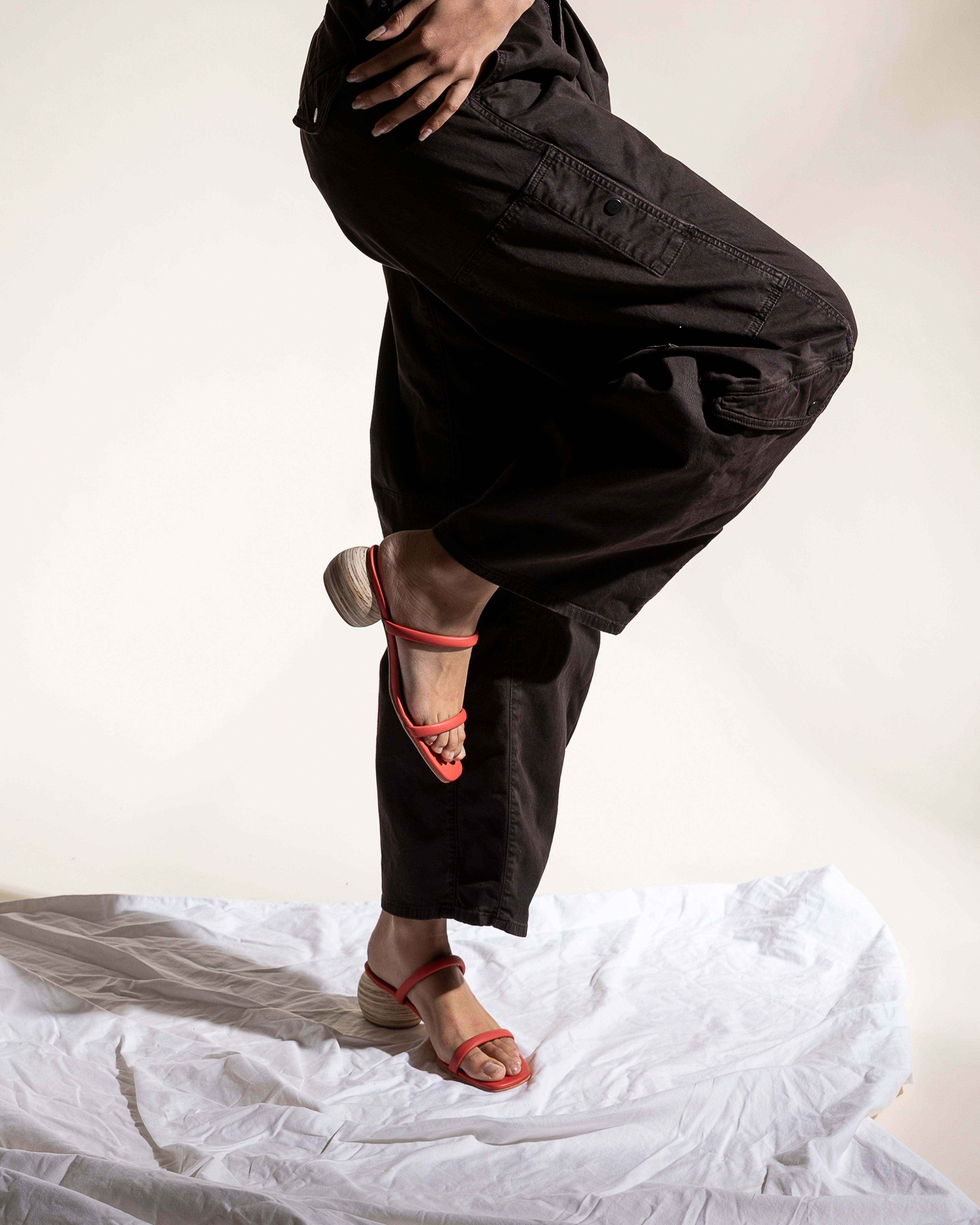 Person wearing black pants and red sandals on a white surface with a neutral background