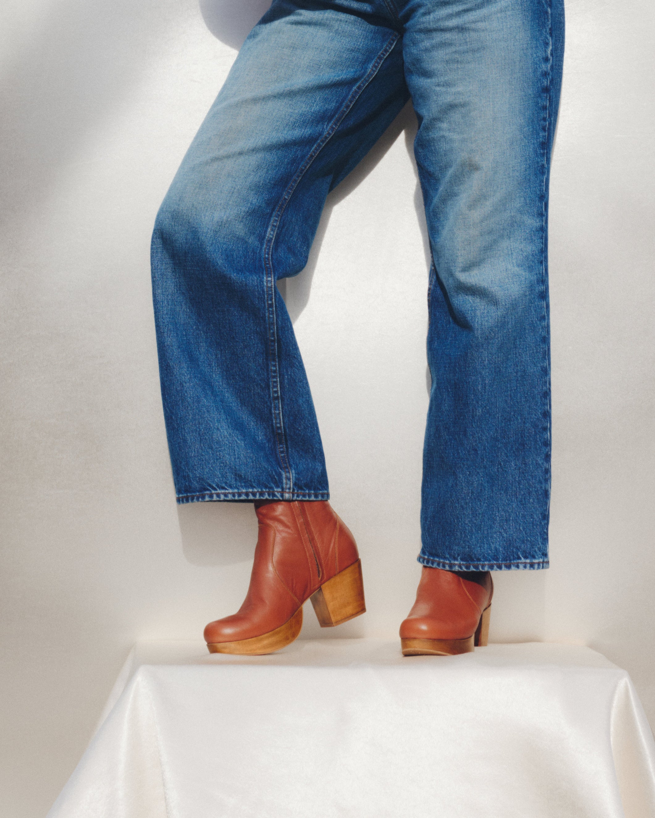Person wearing blue jeans and brown boots on a white background