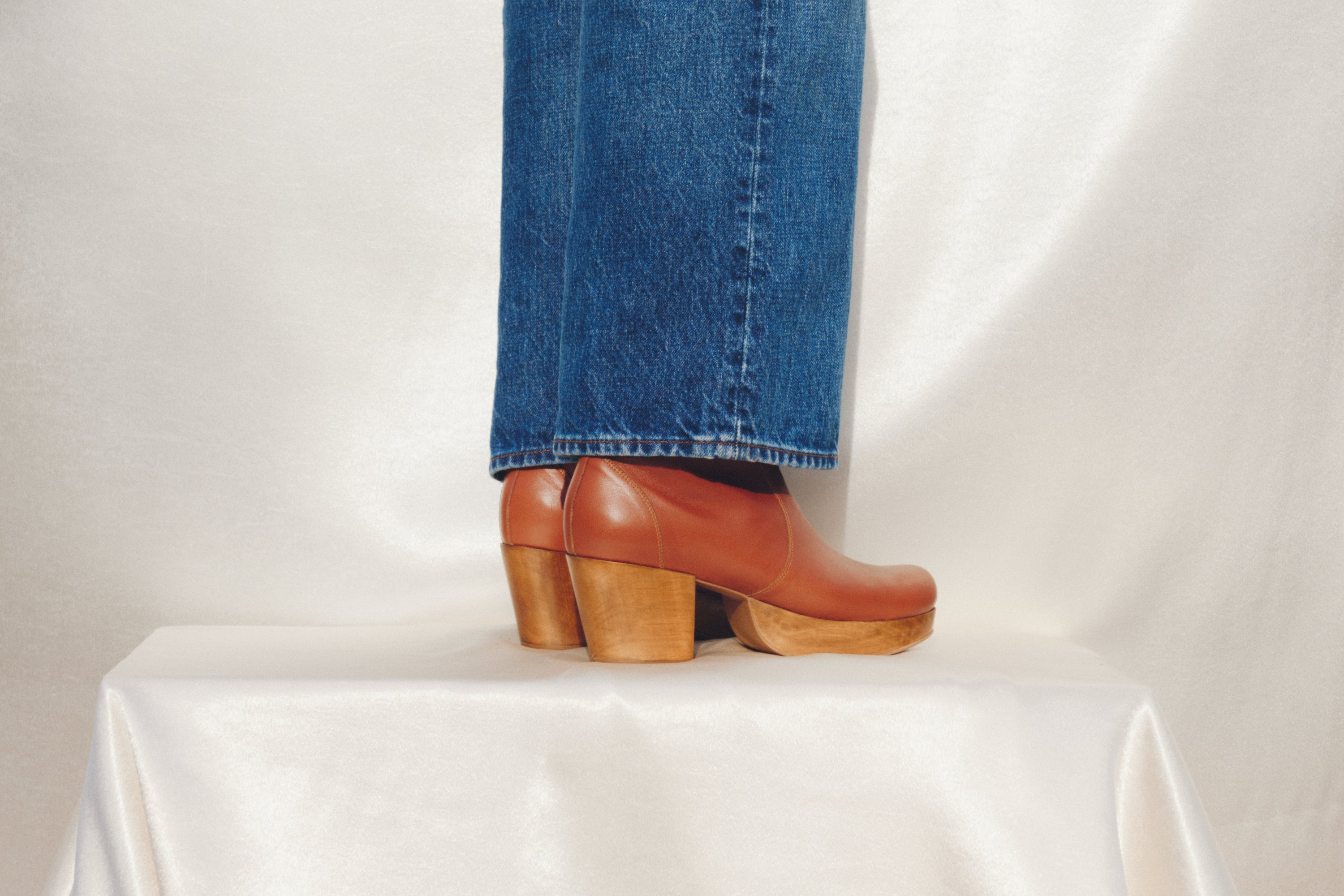 Brown clog boots with wood heels worn with blue jeans on a white background