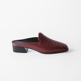 A single burgundy woven leather mule loafer with a low black block heel, shown from a side profile on a clean white background.