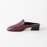 A single burgundy leather mule slip-on shoe with a woven basket-texture toe and a low black block heel, shown in profile against a clean white background.