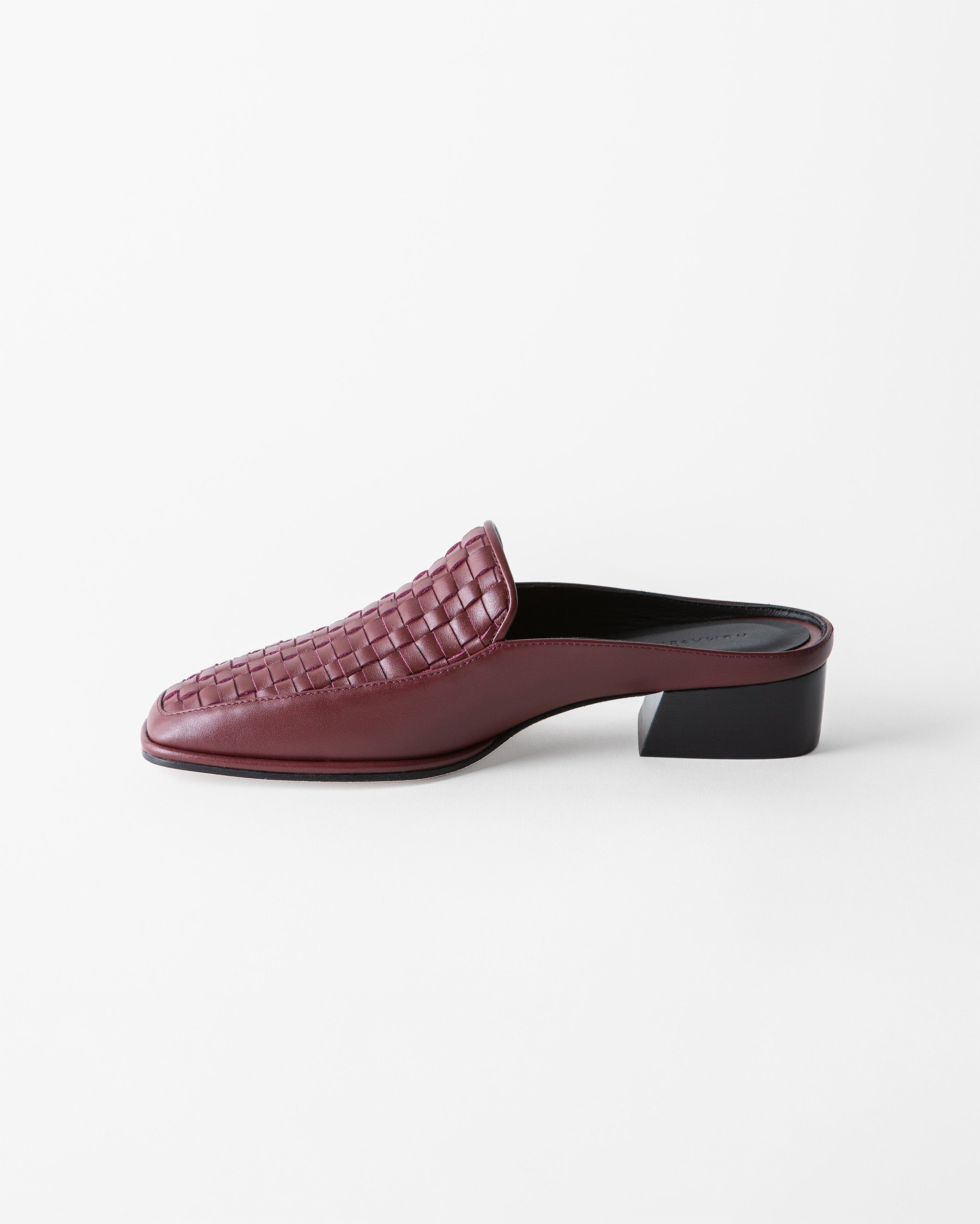 A single burgundy leather mule slip-on shoe with a woven basket-texture toe and a low black block heel, shown in profile against a clean white background.