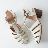 Pair of white sandals with brown soles on a light gray background