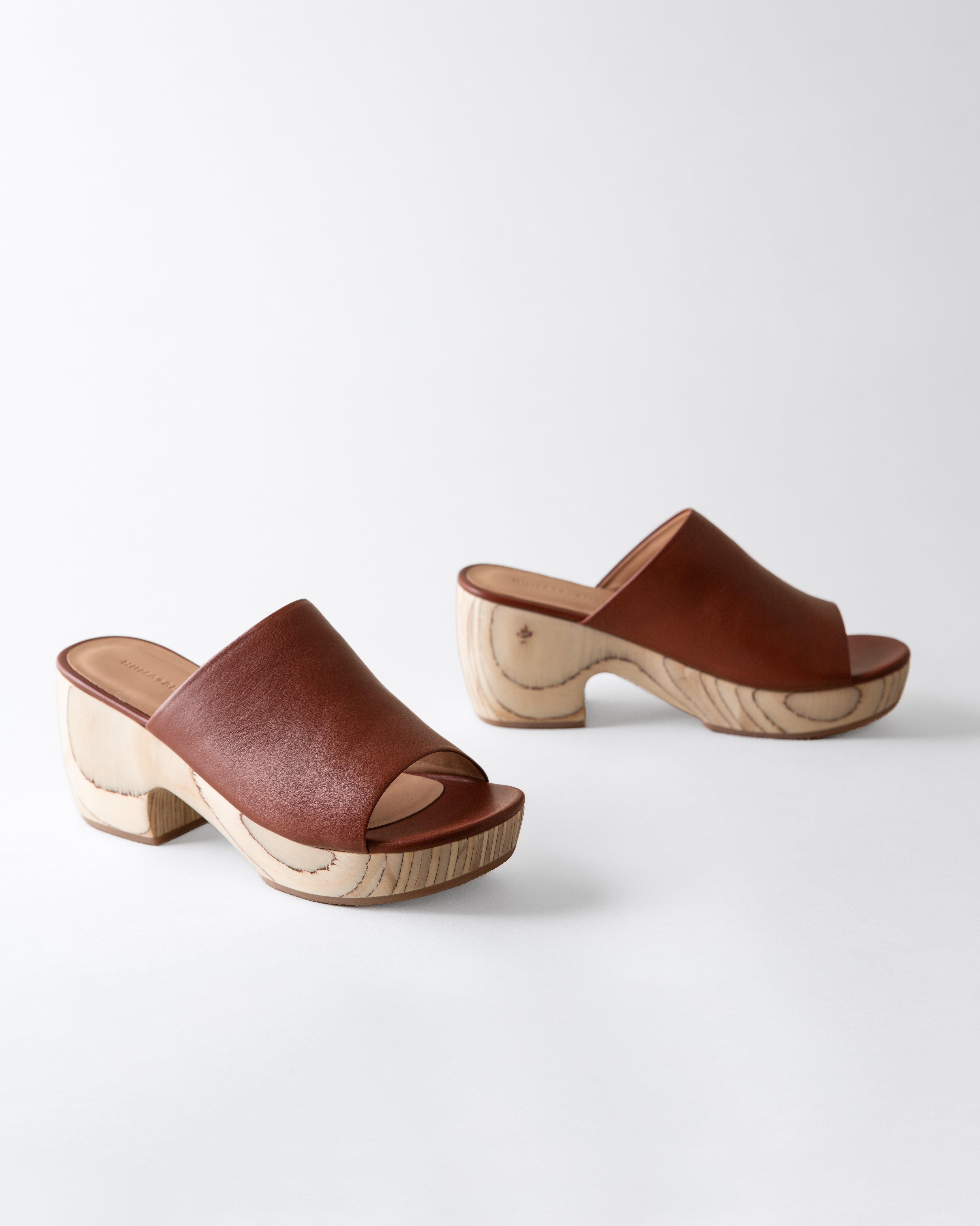 Pair of brown leather clogs with wooden soles on a white background