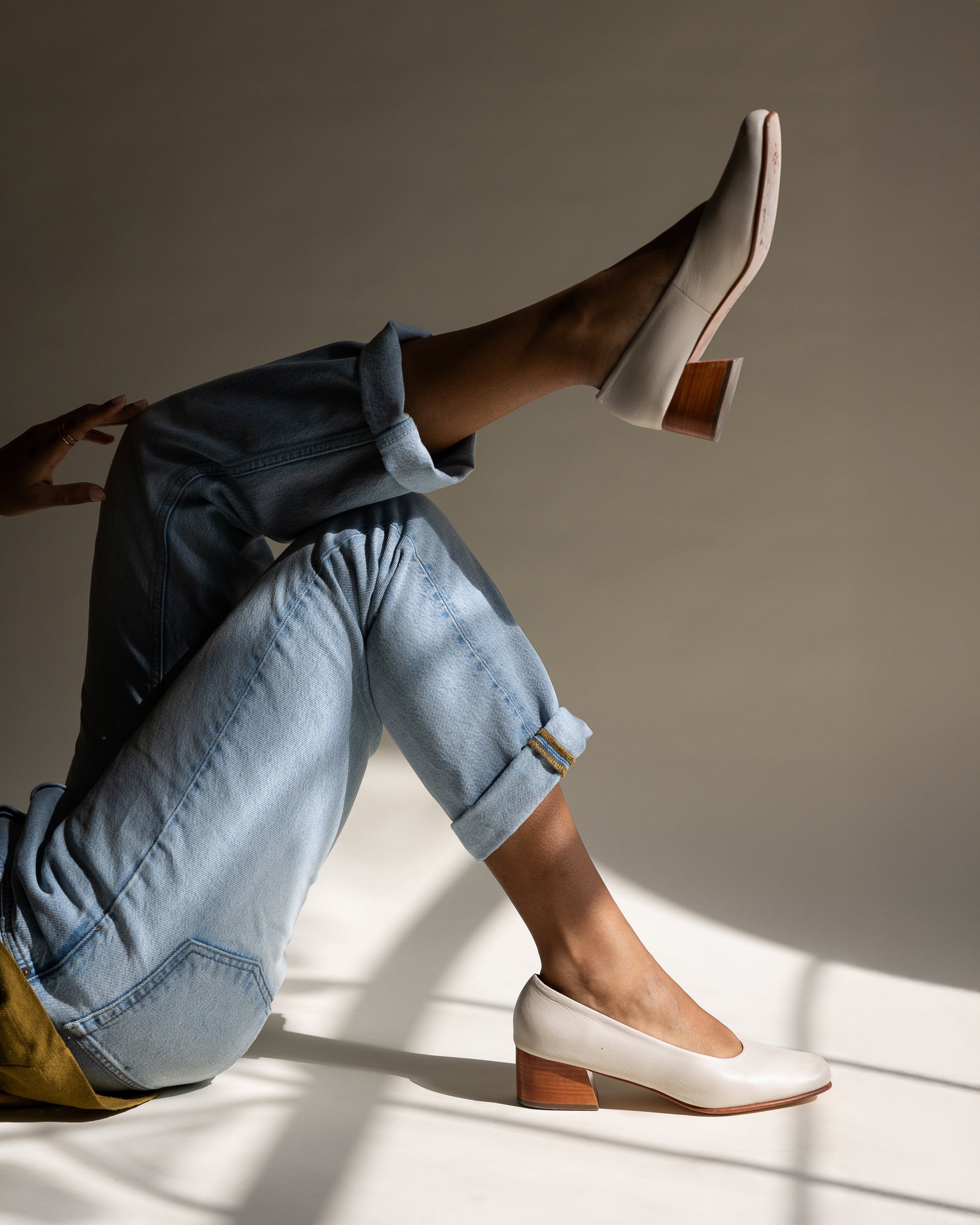 Person wearing light-colored shoes and rolled-up jeans against a neutral background