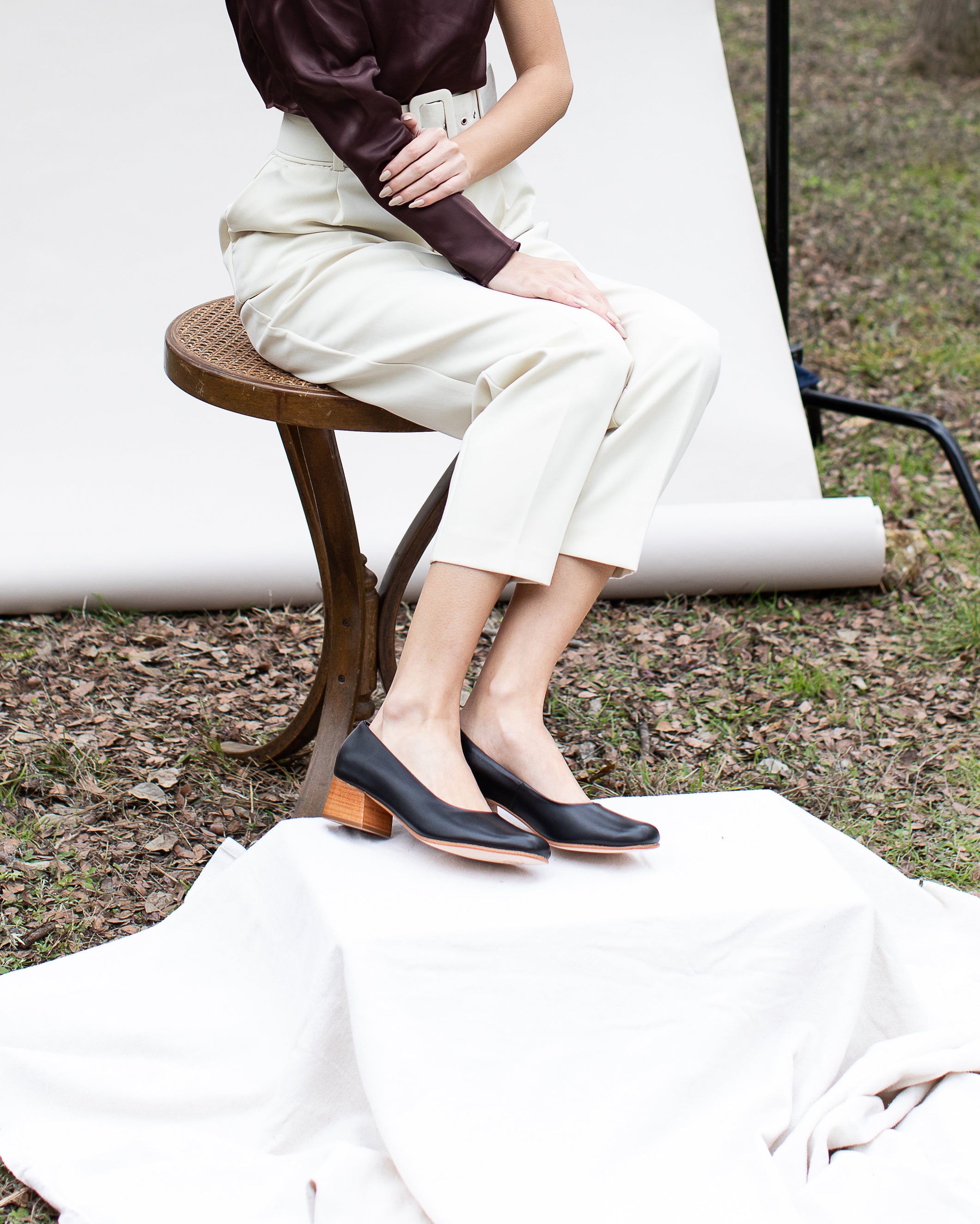 Person wearing black heels sitting on a wooden stool outdoors.