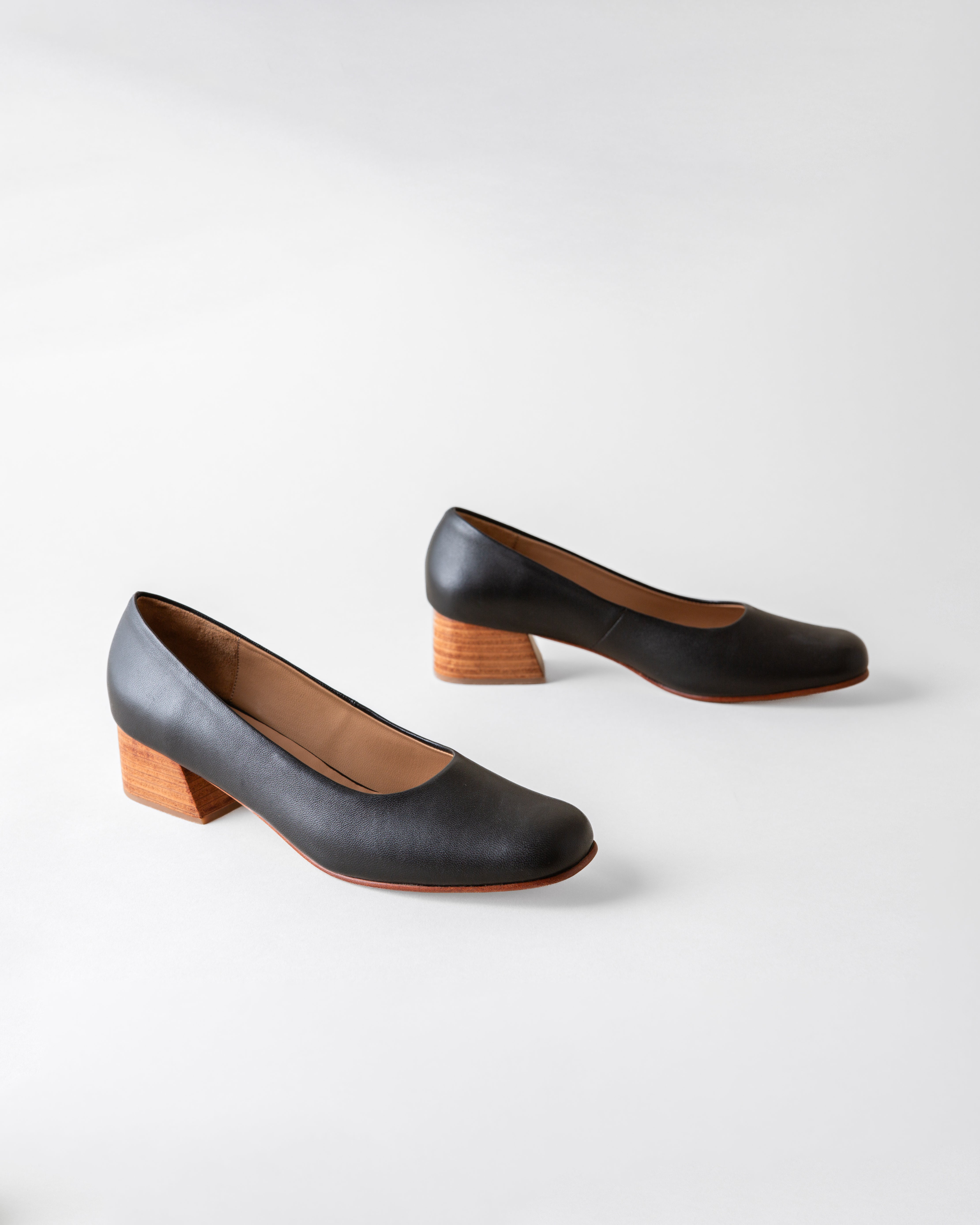 Pair of black leather shoes with wooden soles on a white background