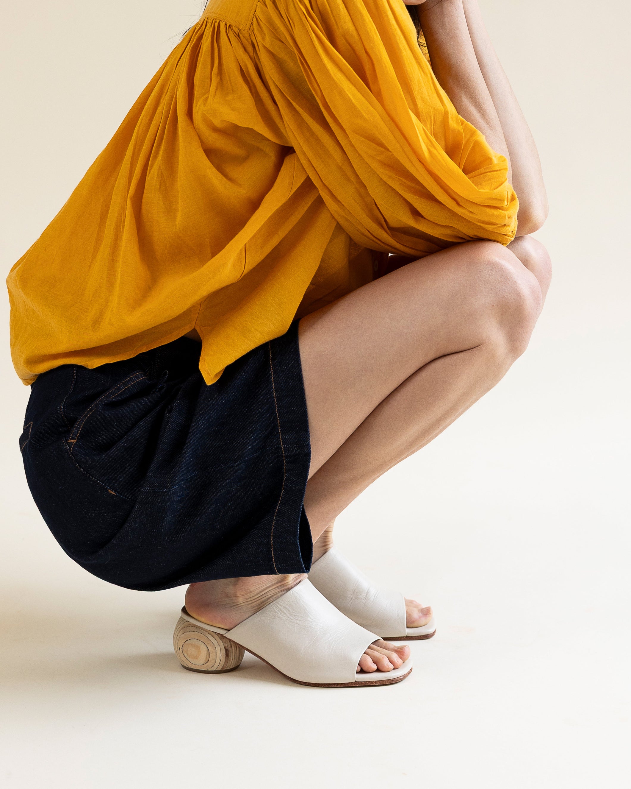 Person wearing a yellow top and black shorts with white sandals on a beige background