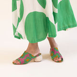 Person wearing green and white patterned pants with colorful sandals on a white background
