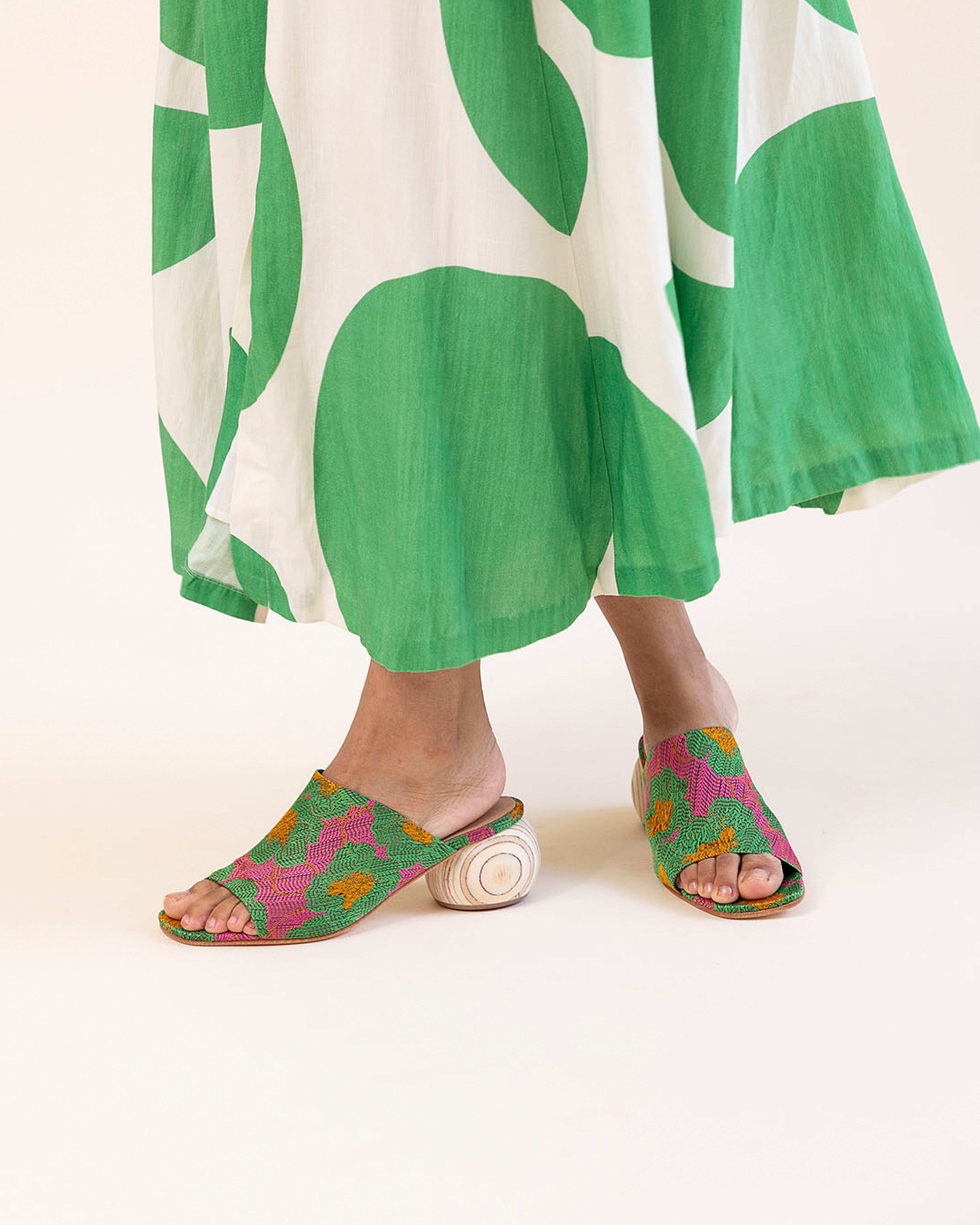 Person wearing green and white patterned pants with colorful sandals on a white background