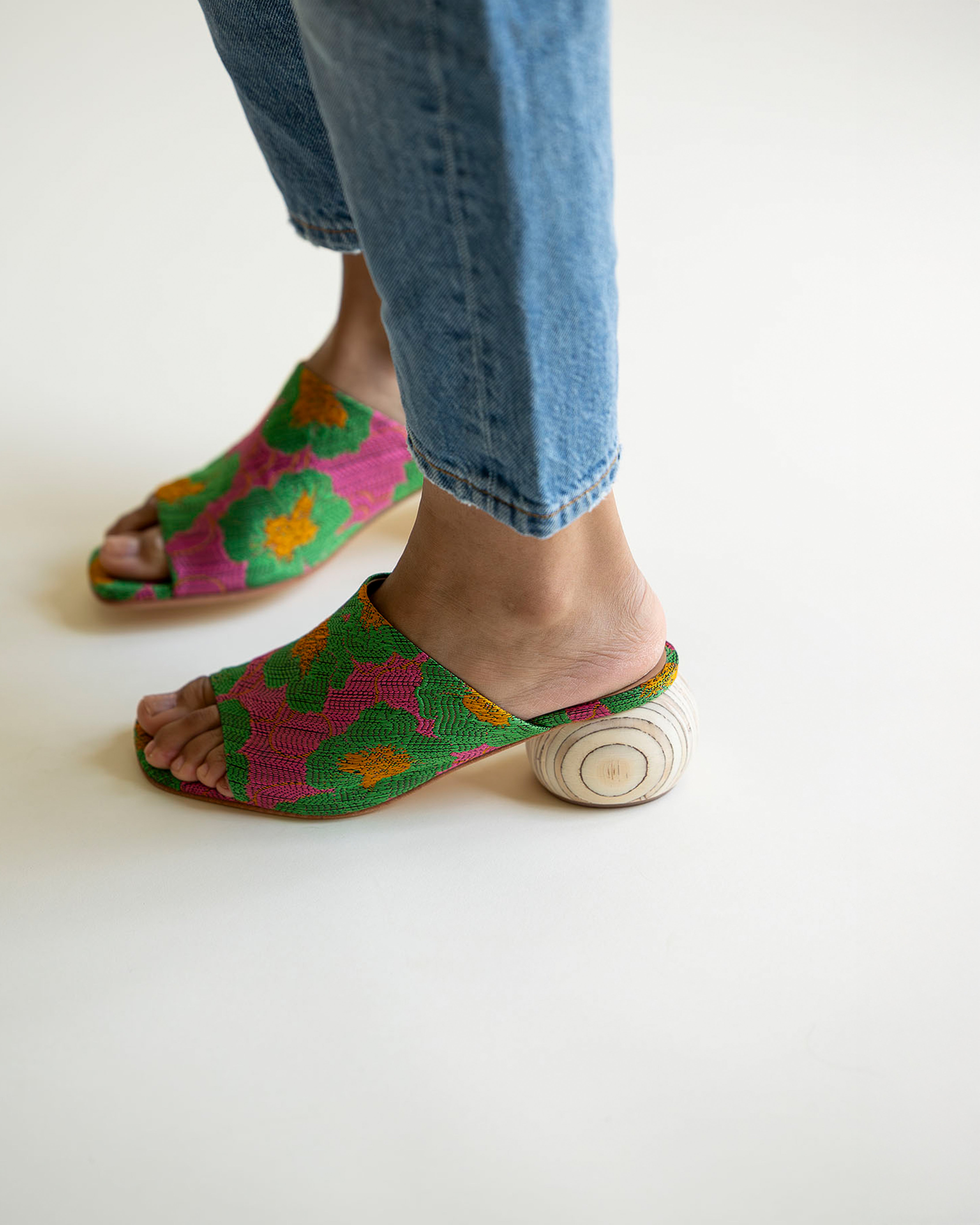 Colorful open-toe shoes worn with blue jeans on a white background
