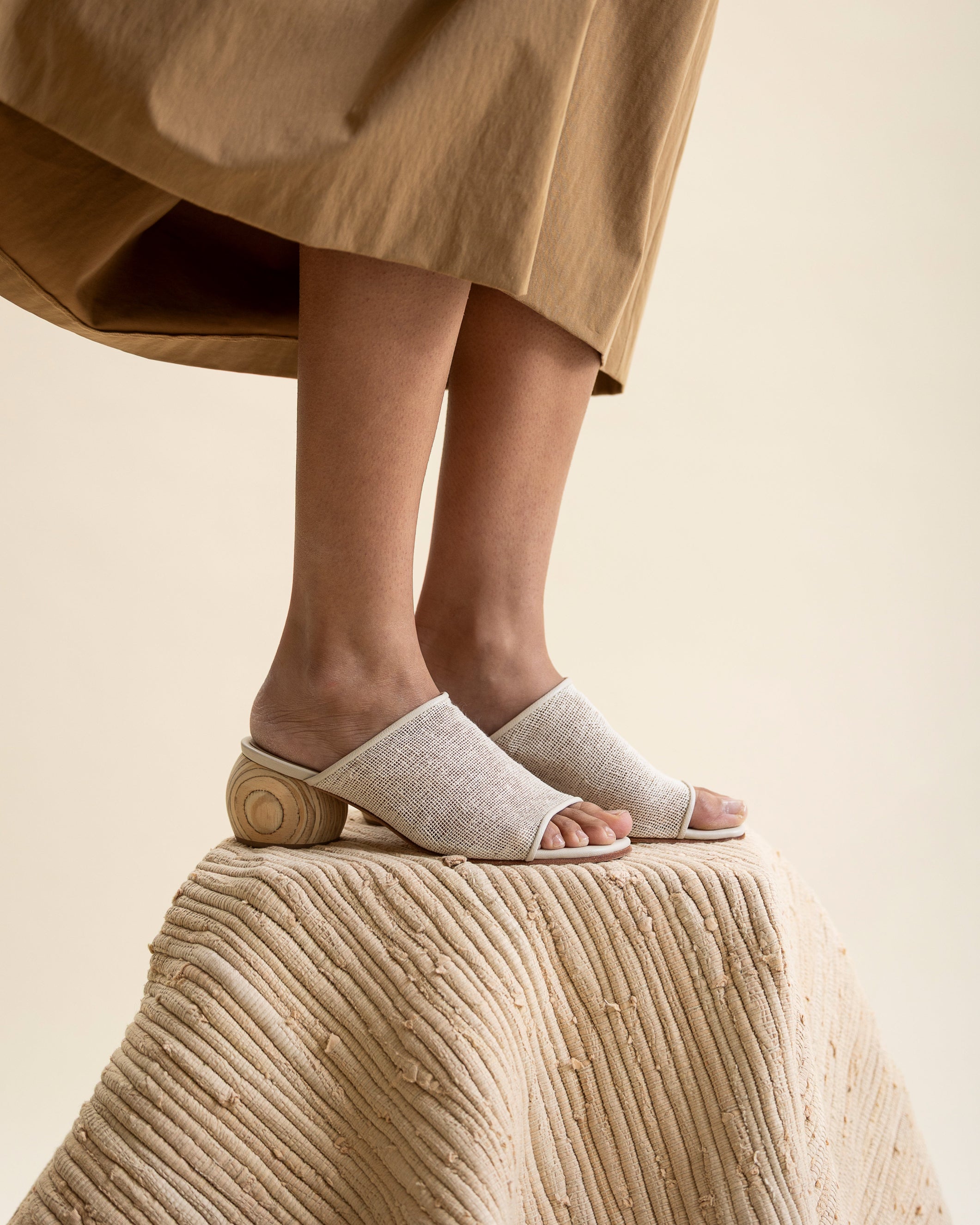 Person wearing white jute open-toe sandals with wooden soles on a beige surface.
