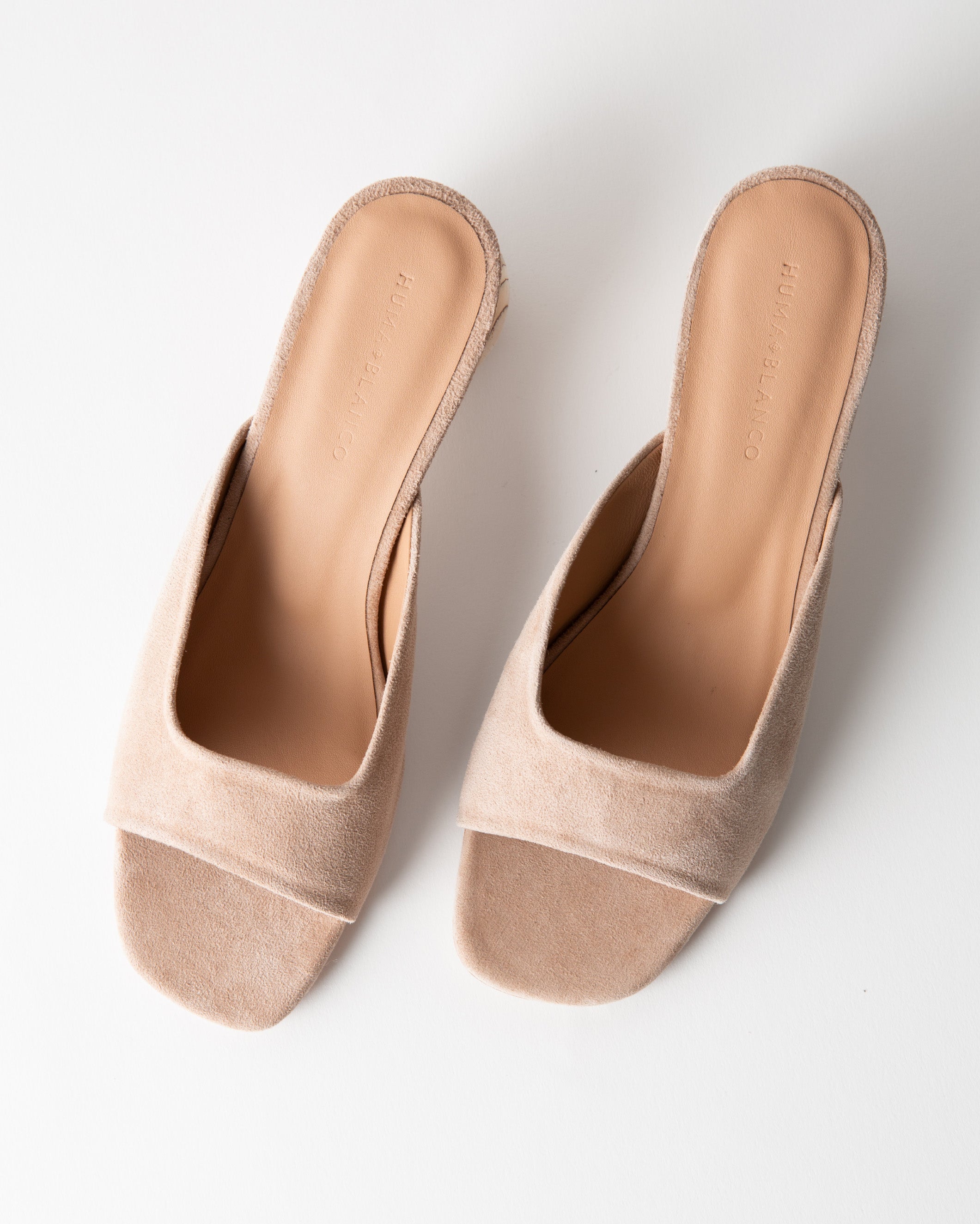 Pair of beige open-toe mules on a white background