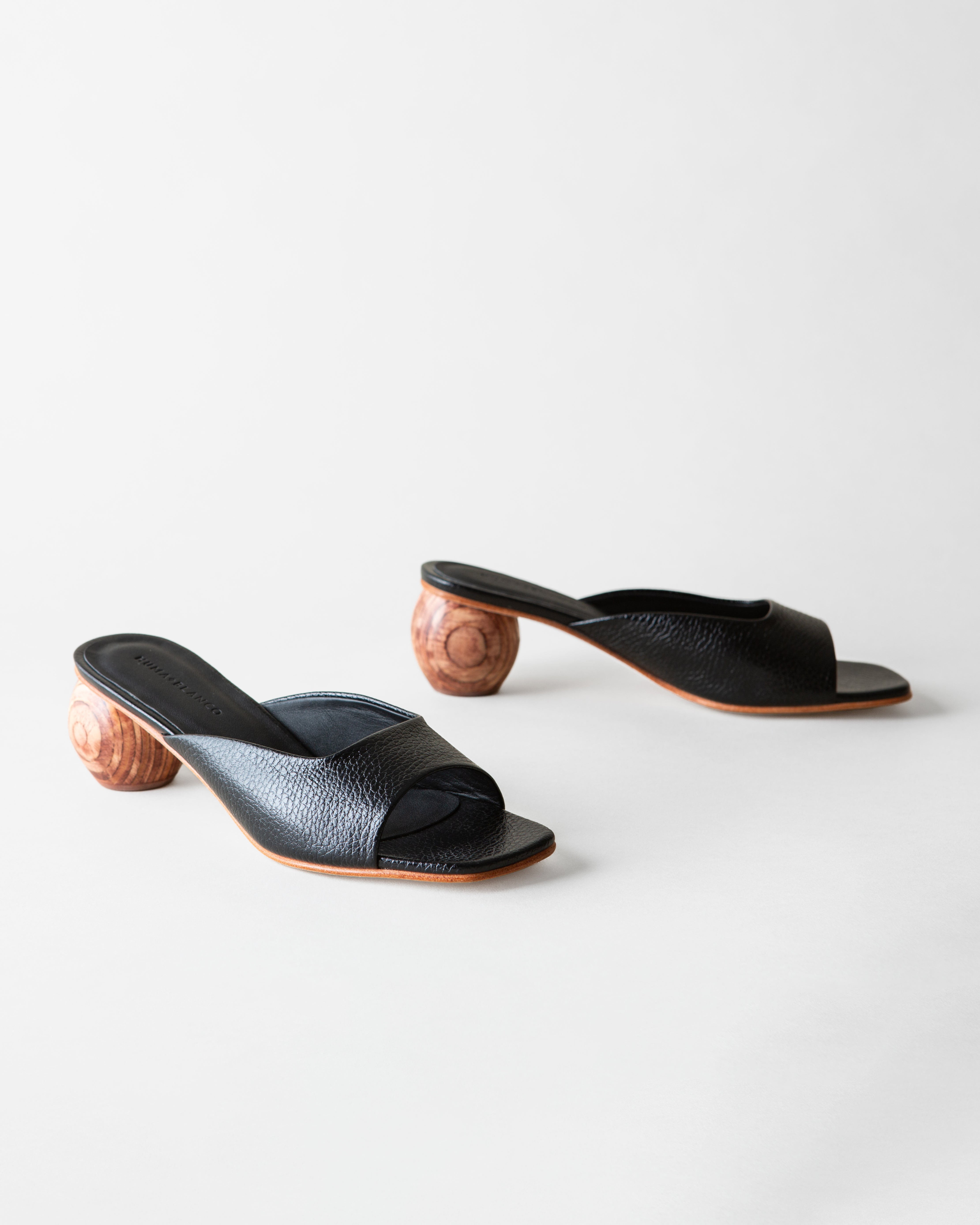 Pair of black open-toe shoes with wooden heels on a white background