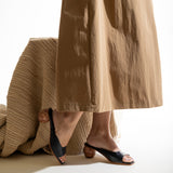 Person wearing a tan skirt and black open-toe sandals with a wood heel.