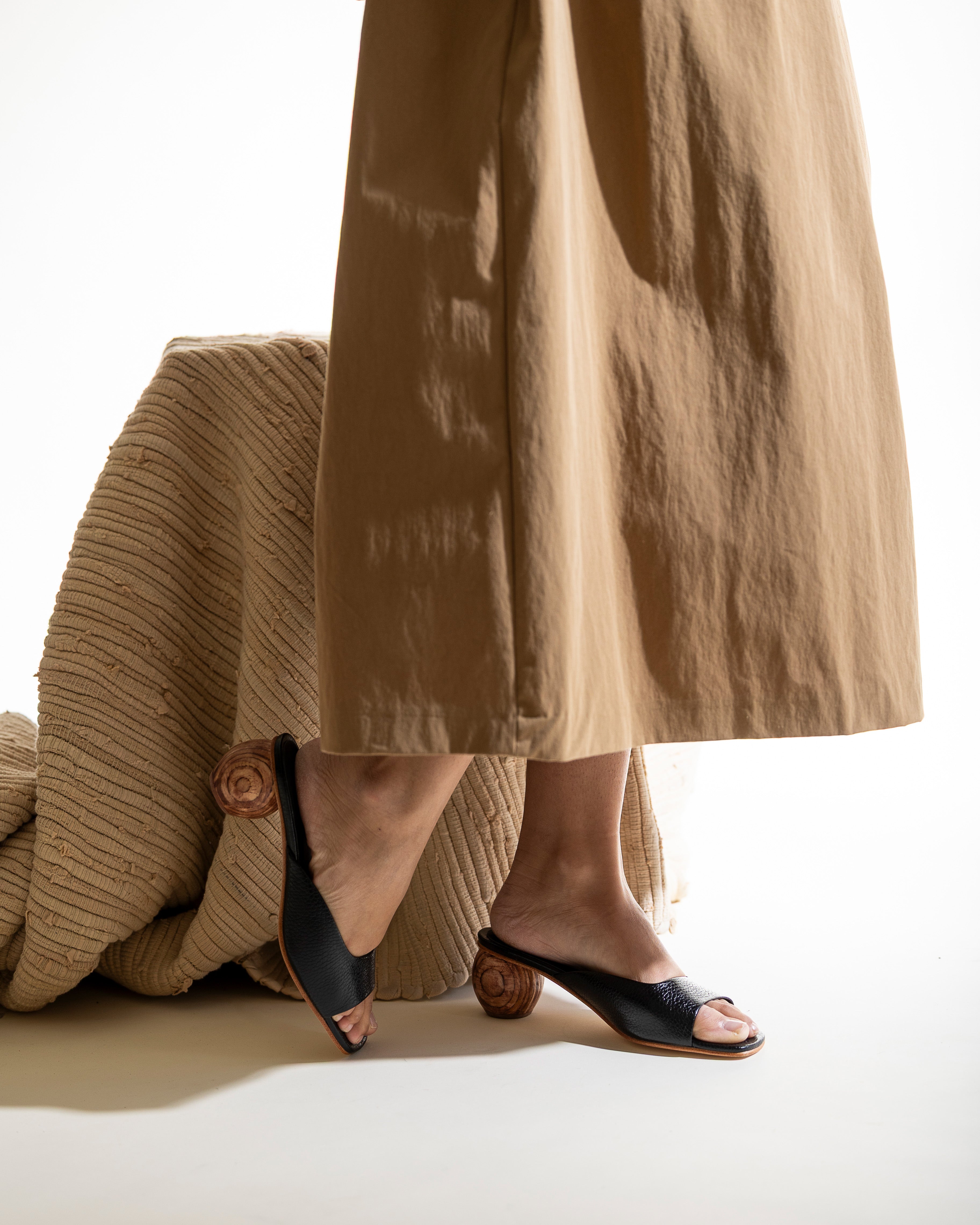 Person wearing a tan skirt and black open-toe sandals with a wood heel.