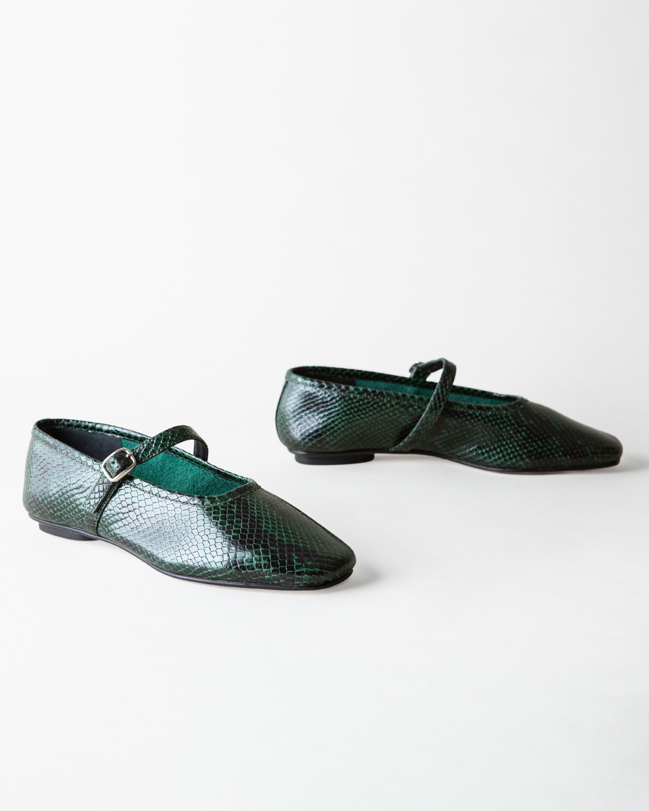 A pair of dark green snakeskin-textured Mary Jane flats with a small silver buckle, displayed on a clean white background.