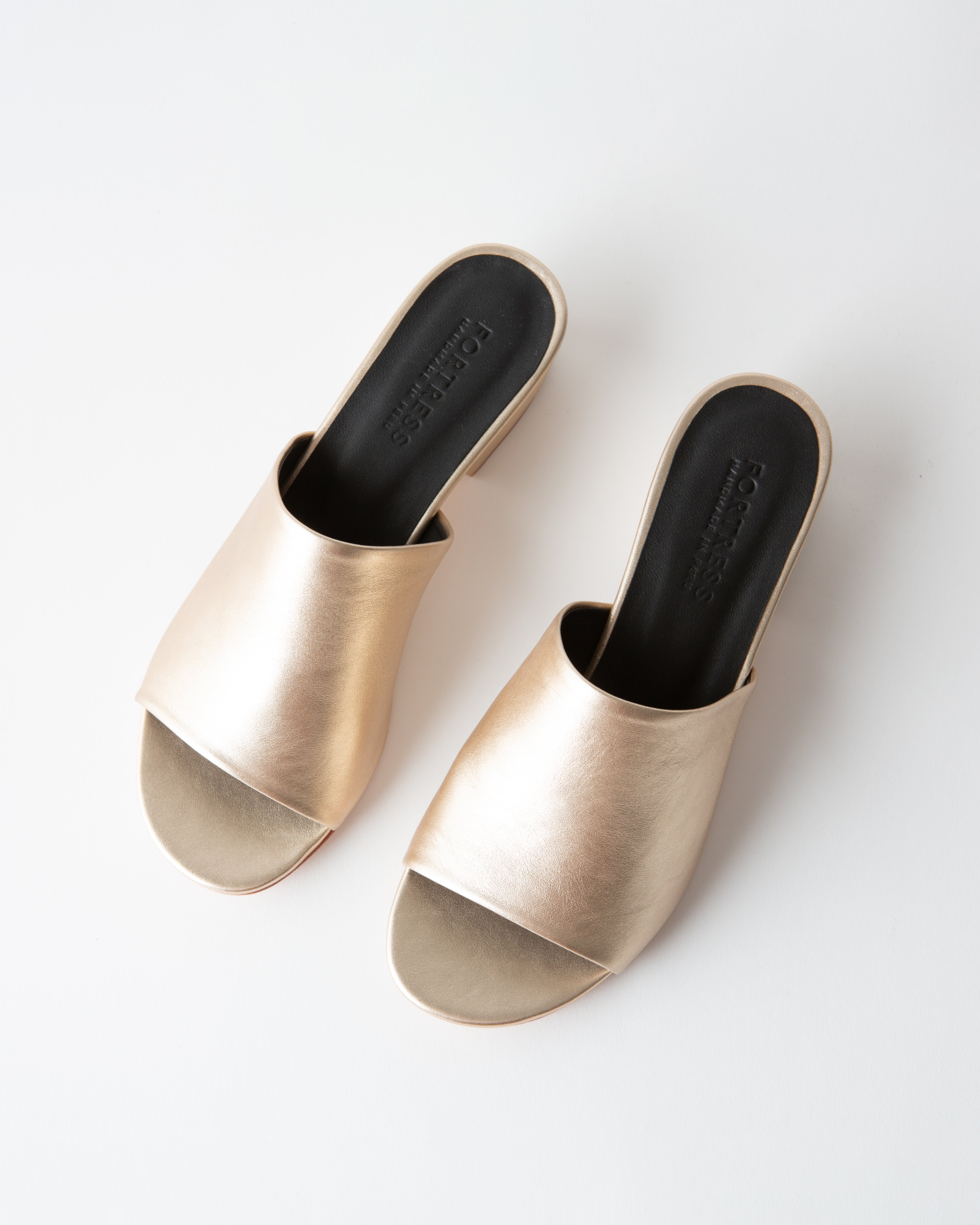 Gold metallic sandals with black insoles on a white background