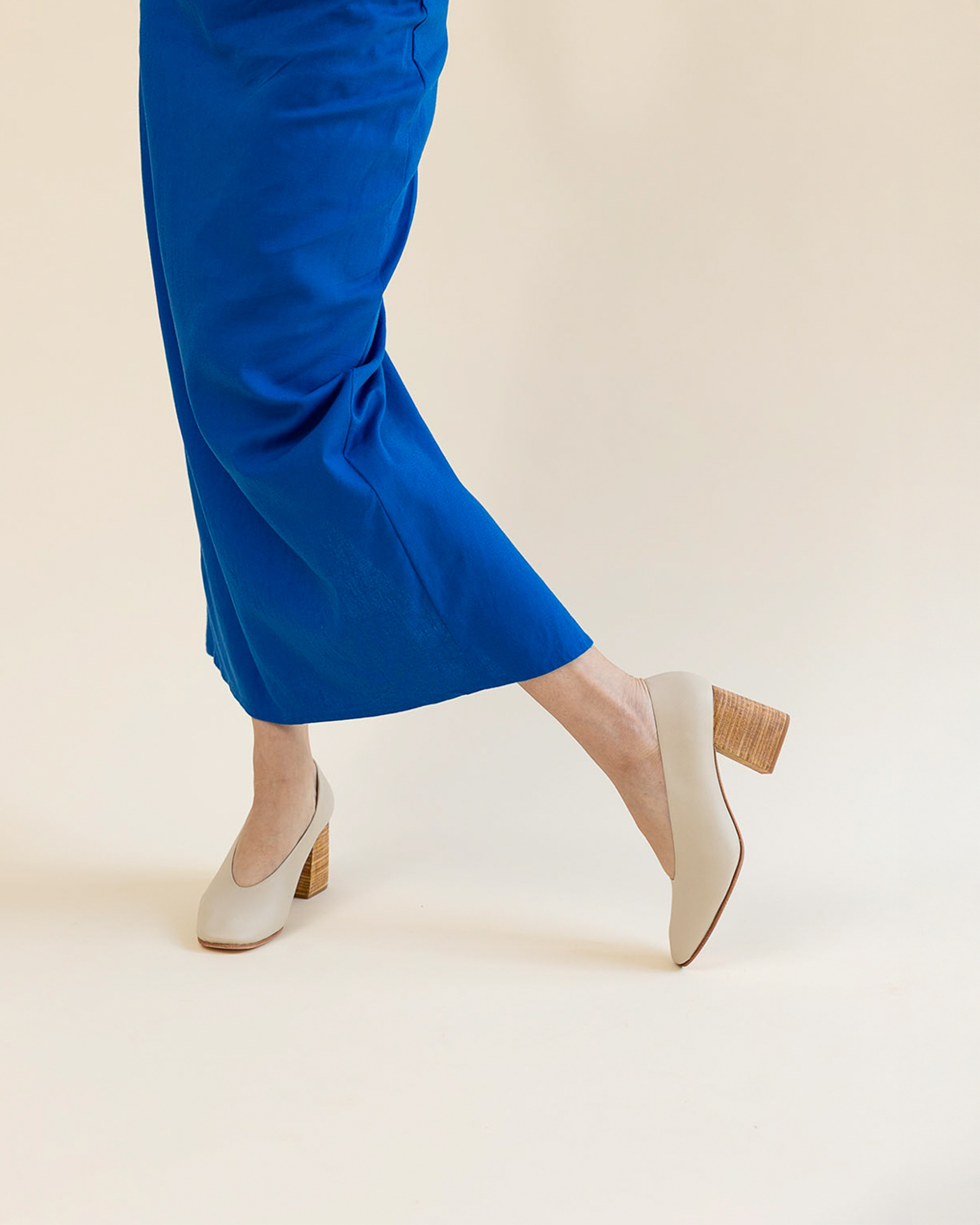 Person wearing a blue dress and light beige shoes on a beige background