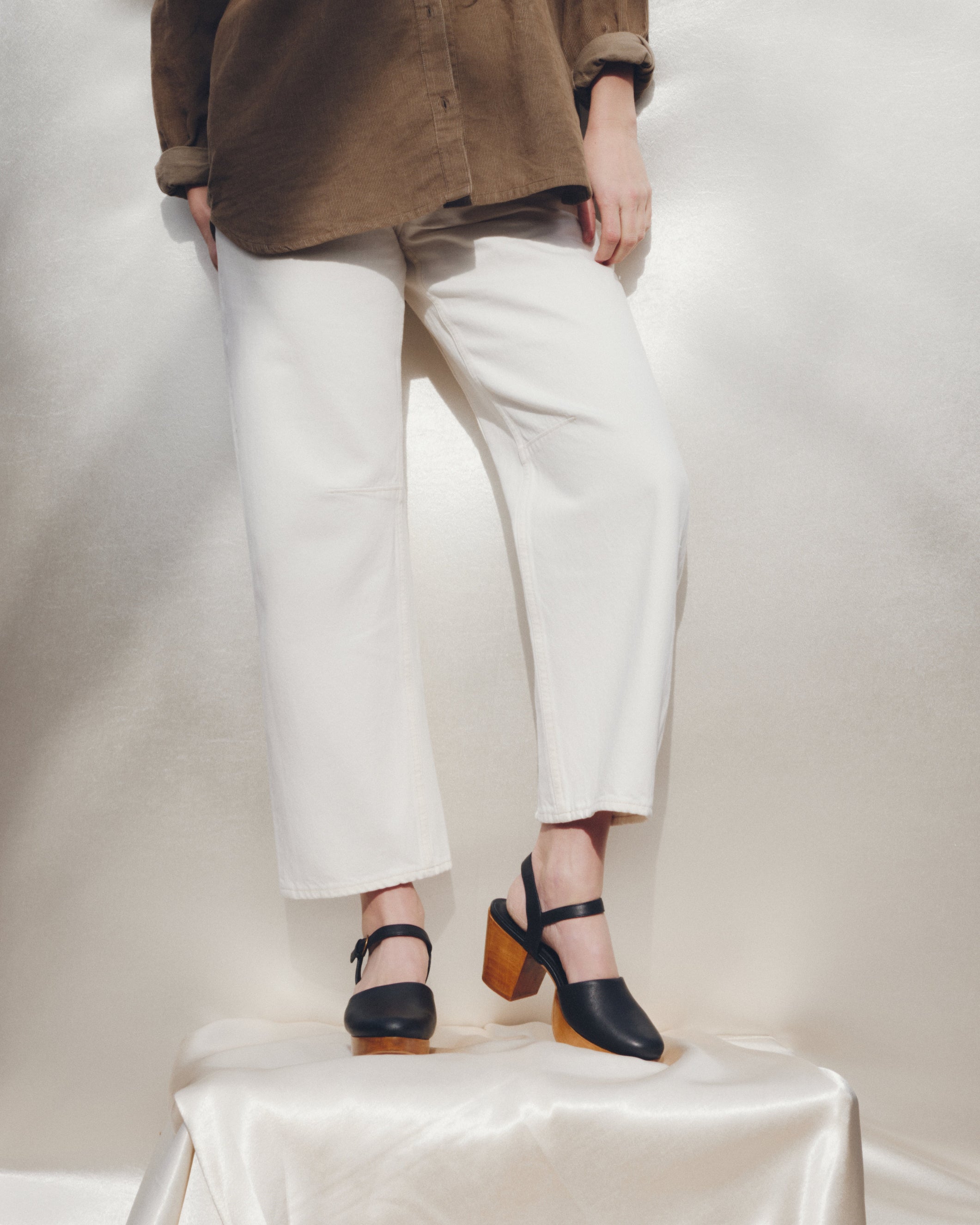 Person wearing white pants and black shoes on a white platform with a neutral background