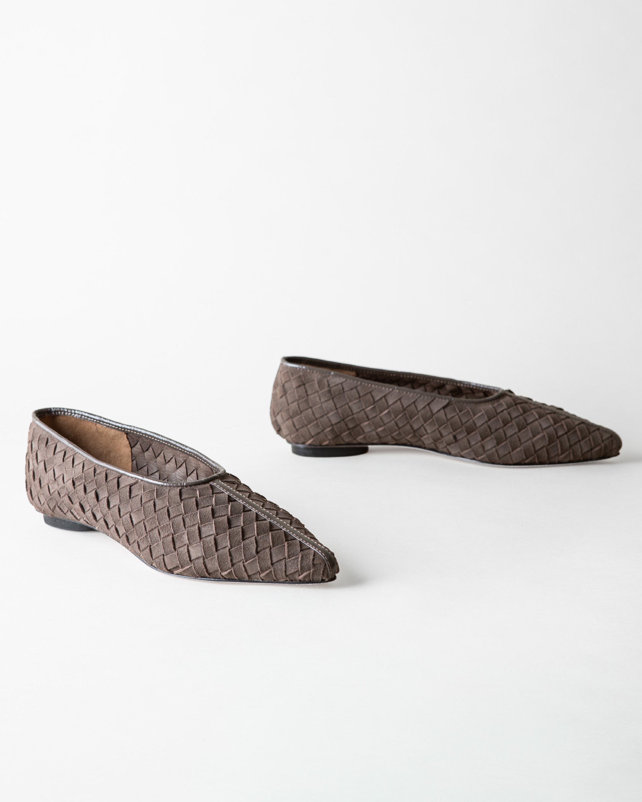 A pair of pointed-toe flat shoes with a woven basket-like texture in a dark taupe-brown color, displayed on a clean white background.