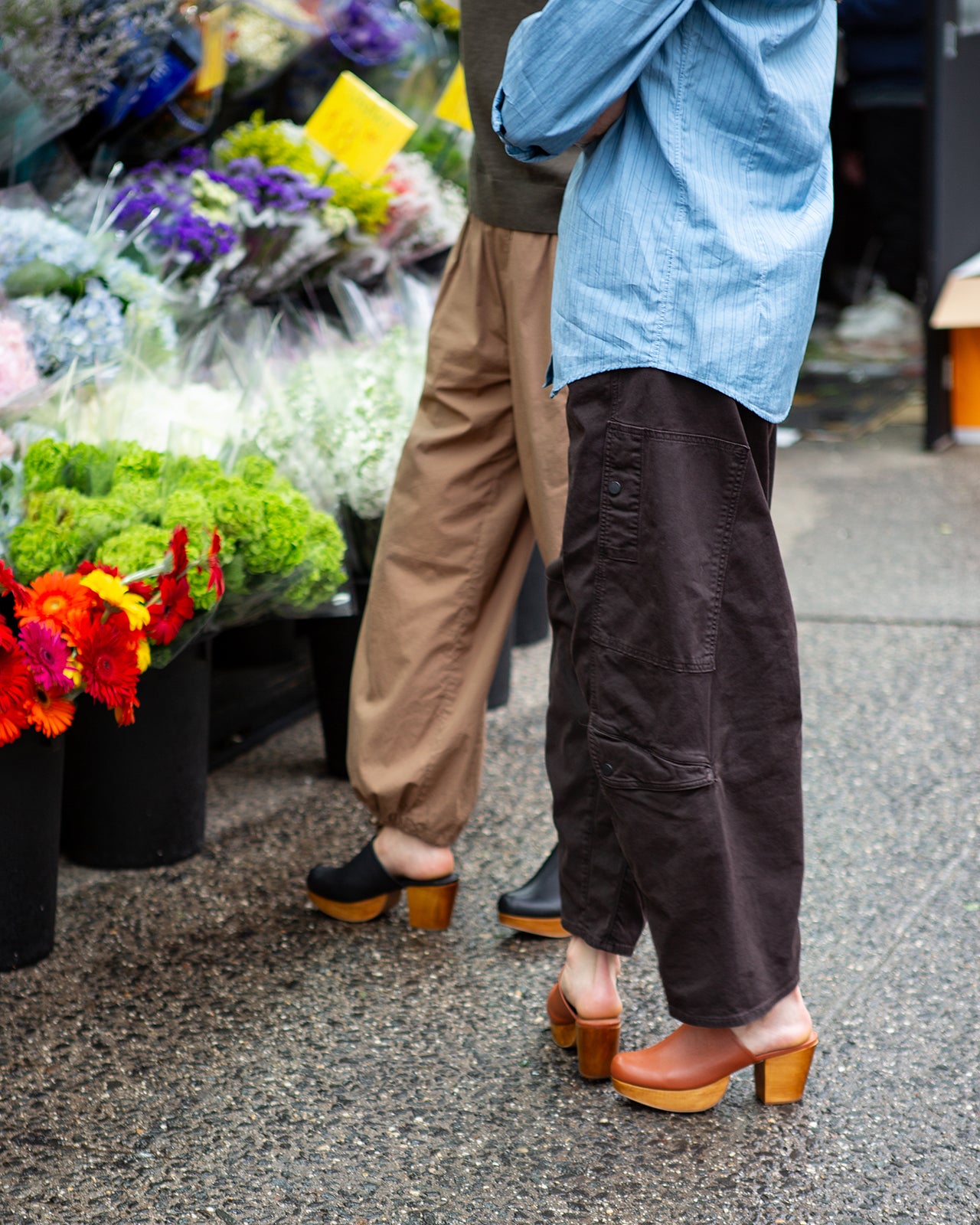 Two images showing a person wearing brown pants and brown leather clogs on a street and a sidewalk.