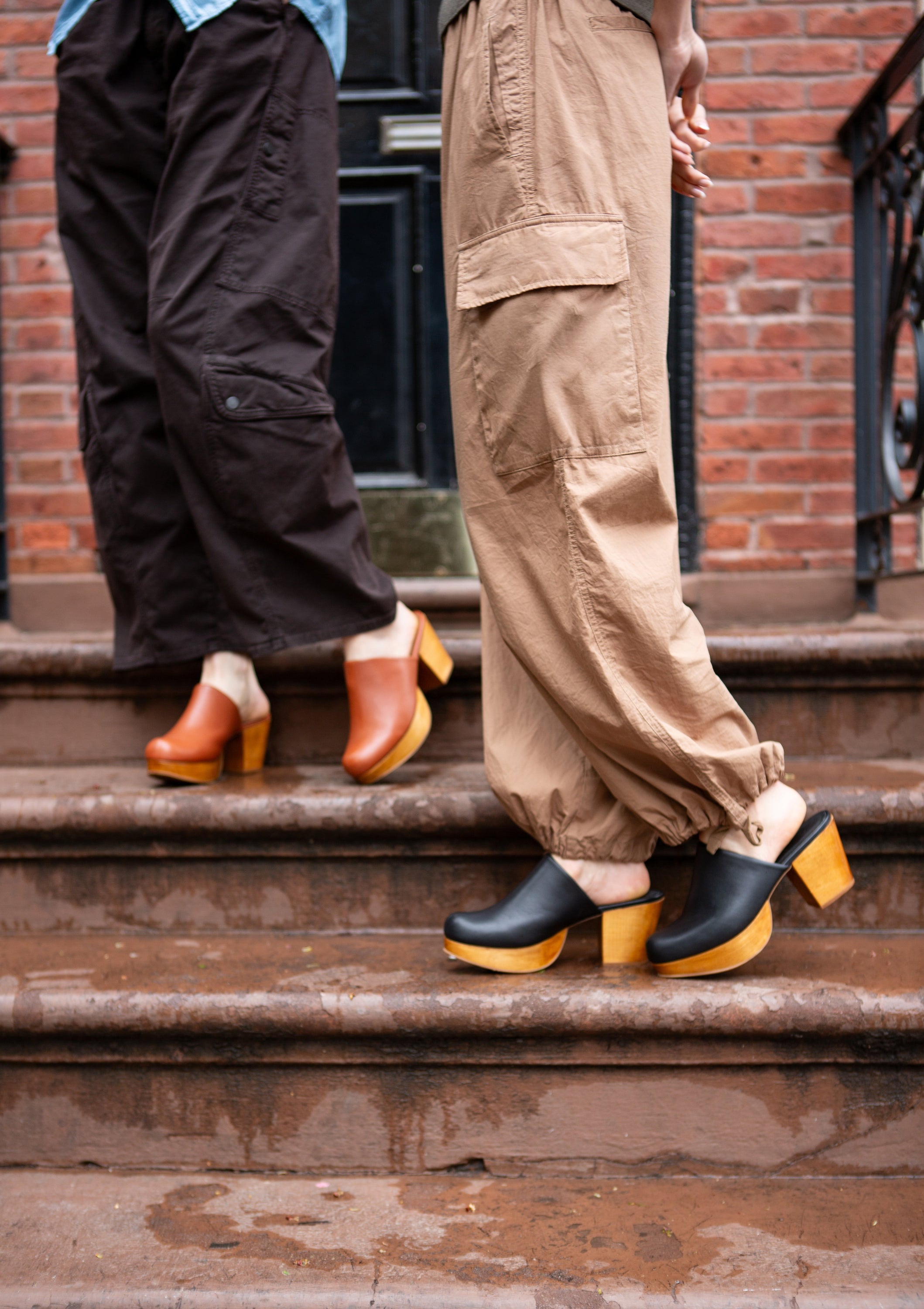 Two people wearing clogs on a brick staircase.