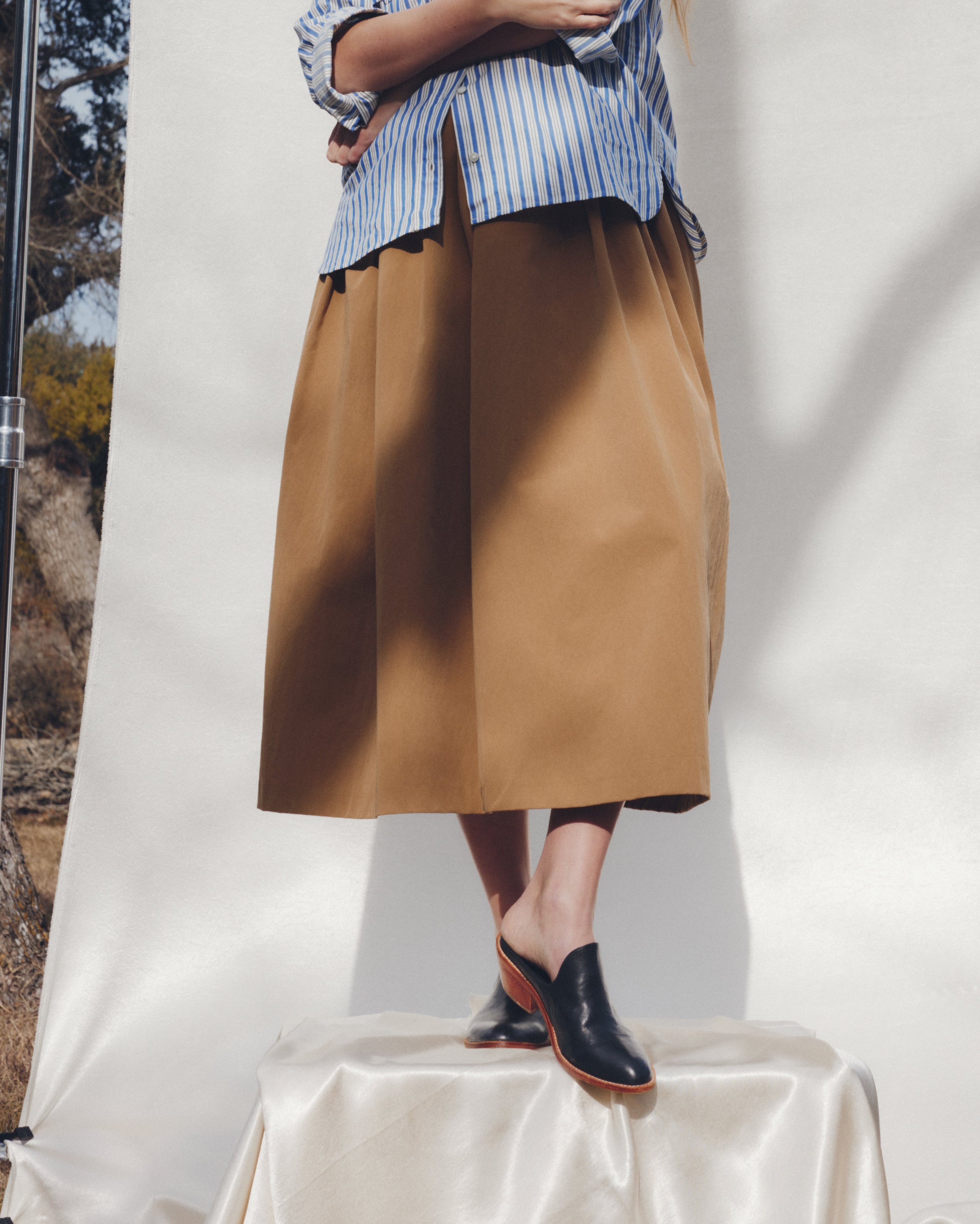 Person wearing a blue and white striped shirt with a brown skirt on a white background