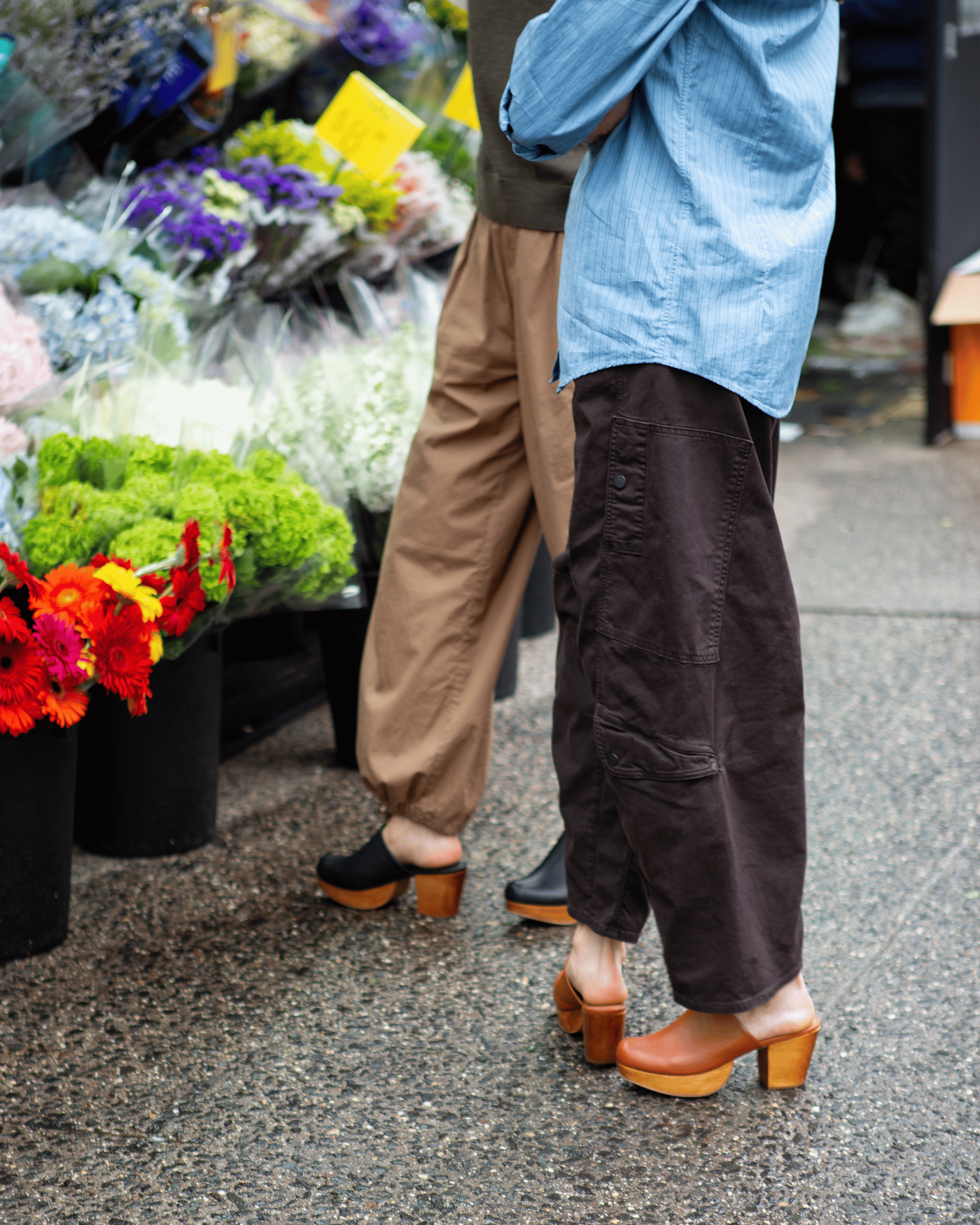Two people wearing clogs standing next to a flower stand with colorful flowers.